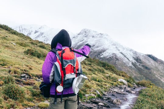 hiker doing a mountain route in winter. She carries a red backpack with shelters and camping utensils. is pointing to his goal. attitude and perseverance.