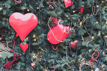 Green spruce branches decorated for Christmas with Christmas decorations in the shape of hearts. Matte toning.