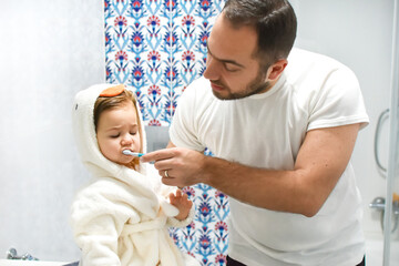 Family father and baby brushing teeth in bathroom. Beautiful child and morning dental hygiene in bath. Kids toothbrush. Dad teaching daughter teeth brushing. Healthy lifestyle.