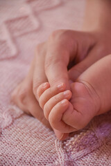 Newborn girl baby holding mother's finger on pink background. Concept of love and family relationship
