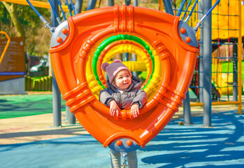 Fototapeta na wymiar Cute adorable baby girl playing on playground in park (garden) Happy family moments concept. Family time. Outdoor activity at a playground in a spring or autumn days. Happy childhood.