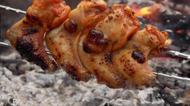 Delicious marinated chicken wings on the skewers are rotating above the open fire outdoors