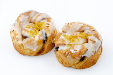 Obraz na płótnie Canvas Two twisted lemon and sultana Danish pastries covered with flavoured icing and lemon shred.