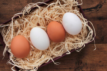 Eggs in wood shavings.  Overhead view of white and brown chicken eggs on wooden table.