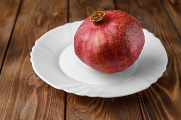 A fresh ripe pomegranate lies on a white saucer on a brown Board. Top view of the grenade.