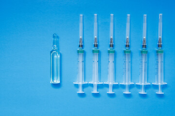 An ampoule with a vaccine and syringes on a blue background. The concept of vaccination against coronavirus.
