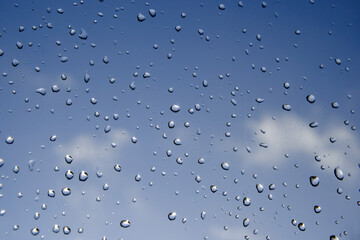 Large rain drops on the window glass with dark blue sky and clouds. Selective focus.