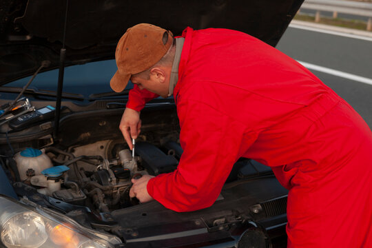 A mechanic in a work suit fixes a malfunction on the car's engine