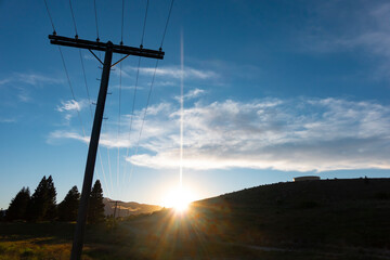 Sun flare through distant hills with power lines glistening in sun and stretching into distance