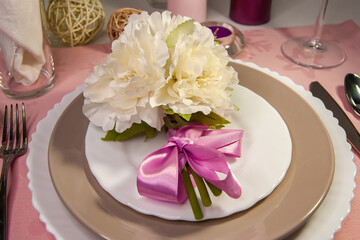 A wonderful white bouquet of flowers with a satin pink ribbon on the plates near the cutlery next to a crystal glass, candles and festive decor. Table setting.