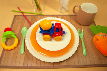 Children's table setting. Three children's plates on a wooden napkin with a plastic spoon and fork, a Cup, tubes and bright toys. The first solid foods.