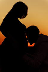 Silhouettes of lovely couple, overjoyed husband kiss pregnant tummy of beautiful wife, young family expect for a baby, excited about parenthood, tender moments concept