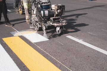 a team of workers drawing a pedestrian crossing in early spring using automated equipment on fresh asphalt