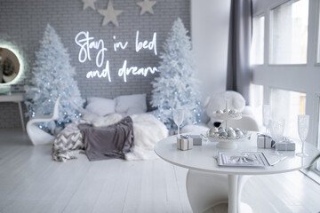 Christmas gray bedroom interior with modern comfortable bed and Christmas trees. Festively decorated table with glasses, cutlery in white, silver colors. Holiday background. Christmas concept