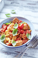 Farfalle pasta with chicken breast, cherry tomatoes and fresh basil. Bright wooden background. Close up. 