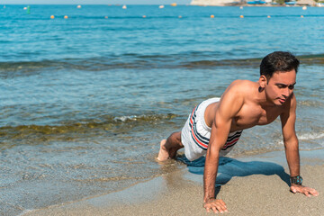 Young handsome man does push-ups on the beach in the morning