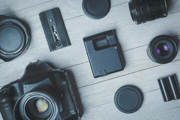 Flat lay with different black photoaccessories on light boards: camera, lenses, battery, charger, synchronizer, and lens covers
