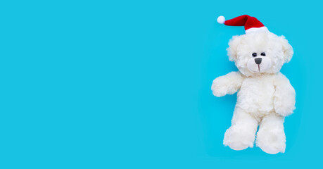 Toy bear wearing a santa hat on blue background. Christmas holidays concept