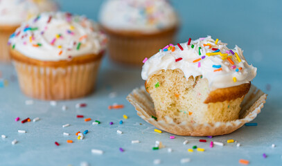 Close up of a half eaten cupcake with white frosting and sprinkles.
