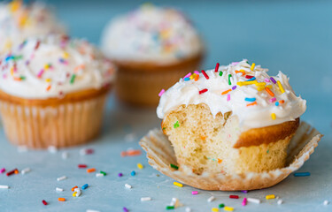 Close up of a half eaten cupcake with white frosting and sprinkles.