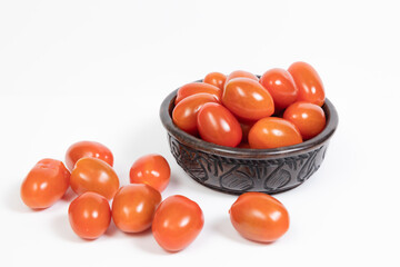 Cherry tomatoes in an African ebony wood bowl on a white background. Some cherry are fallen on the table. concept vegetable, cooking, healty nutrition,