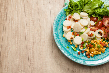 Fresh and exquisite salad of palm hearts cut into slices, cherry tomatoes, corn kernels, red pepper, lettuce in a vintage light blue plate on a wooden table ready to taste. concept healty food.