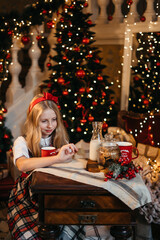 Good New Year spirit. Little blonde girl sitting near a Christmas tree with a gift waiting for Santa