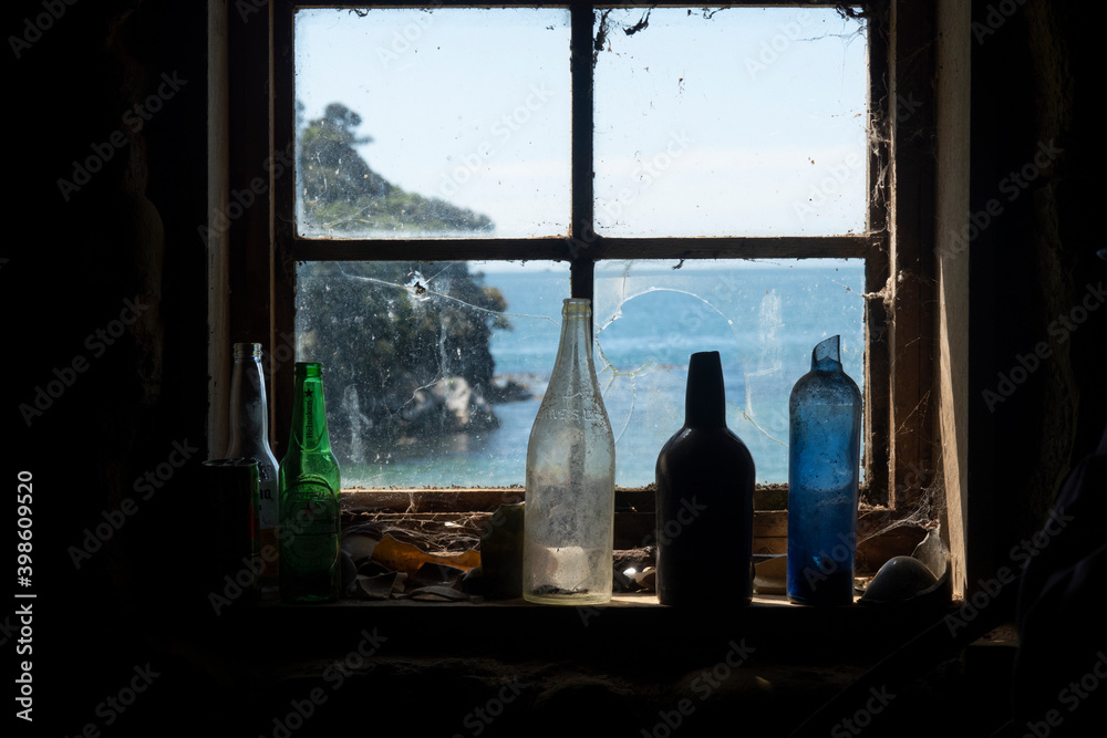 Wall mural Old bottles standing on window sill of multi-paned window with view through to coastal scene