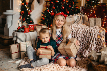 Fototapeta na wymiar Little boy and girl are sitting near the Christmas tree and hugging. Happy brother and sister