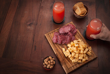 
Food board on wooden table and glasses of snacks seen from above. salami, cheese, french fries, peanuts.