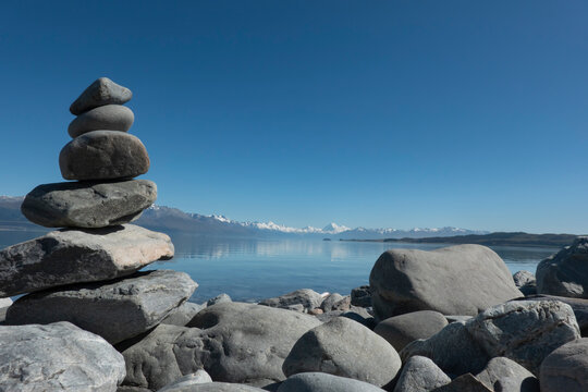 Stone stacks on shore of Lake Pukaki with Southern Alps in distance across lake.