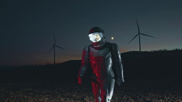 Space mission. Spaceman in special equipment walking on the new uncharted planet at the night while looking asides. Astronaut travel in space during important mission with windmills at the background