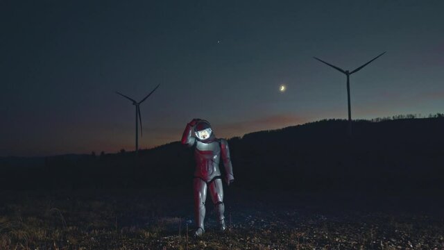 Full length view of the astronaut walking on the surface of planet. Space man in white spacesuit lifts the glass in the helmet while exploring a new planet at the night time. Space exploration concept
