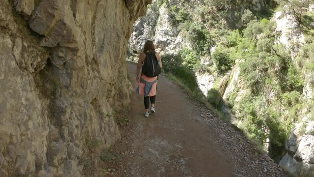 Cain, Spain - September 1, 2020: SLOW MOTION - Female hiking trough the Cares Route in the heart of Picos de Europa National Park, Spain. Narrow and impressive canyon between cliffs, bridges and caves