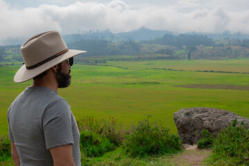 A hispanic man with a hat and beard on vacation in the countryside, surrounded by mountains