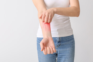 Young allergic woman scratching her skin against light background