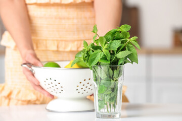 Glass with fresh mint on table and blurred woman with citruses in kitchen