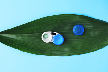 Green leaf and container with contact lenses on color background