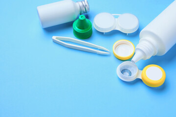 Containers with contact lenses, solutions and tweezers on color background