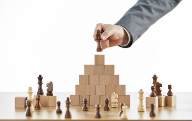 Businessman in a suit arranging chess pieces on wooden blocks on different levels