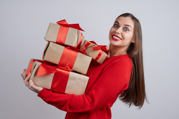Happy young woman in a red sweater holding a few gift box, against gray background. Holiday concept, Christmas, New Year, birthday.