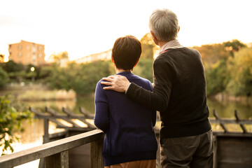 夕日の綺麗な公園で遠くを眺めながら仲良く寄り添う高齢者の夫婦