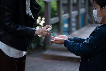 息子の手に消毒液をスプレーする母親