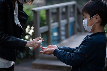 息子の手に消毒液をスプレーする母親