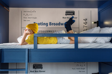Boy in yellow tshirt and hat on blue two-tier bunk bed - obrazy, fototapety, plakaty