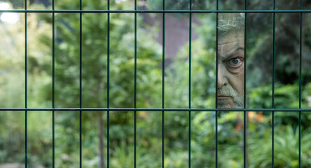 ein getarnter Mann sieht angespannt durch einen Zaun