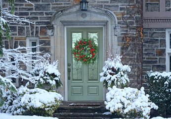Front door with Christmas wreath with red holly berries on old stone faced house