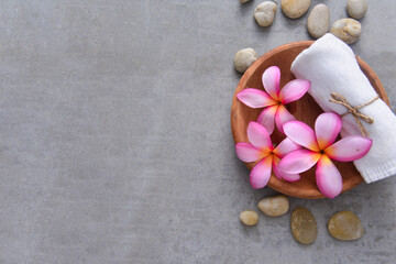 Fototapeta na wymiar Spa composition with pink frangipani flowers and towel, salt in wooden bowl ,stones on grey background 