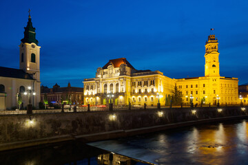 Fototapeta na wymiar Illuminated City Hall on Oradea embankment in twilight, Romania