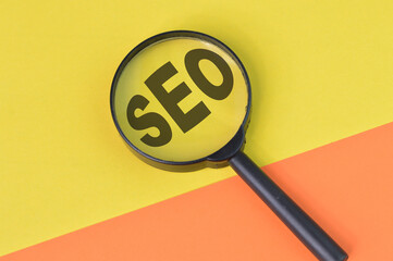 Top view of magnifying glass with text SEO isolated on yellow and orange background. SEO stands for Search Engine Optimization. Business and business concept.